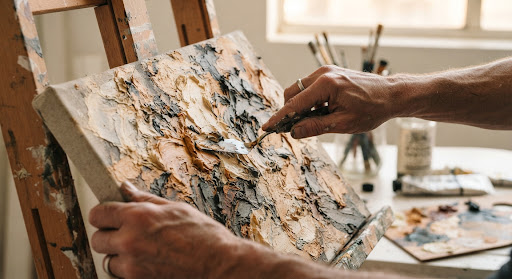 Close-up of Jake Bailey's hands working with a palette knife on a textured acrylic painting
